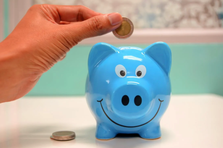 A hand places a coin into a piggy bank
