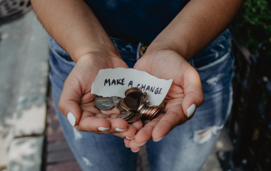 Cupped hands hold loose change and a handwritten note reading "make a change" illustrating the concept of corporate charity fundraising