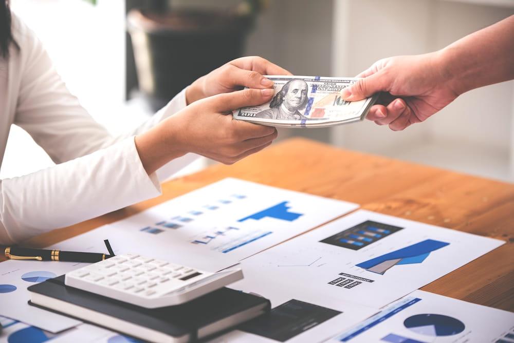 Hands exchanging money over charts to improve workplace giving as a part of a company's payroll giving policy.