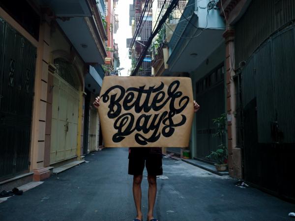 A man holds up a handwritten sign reading "better days"