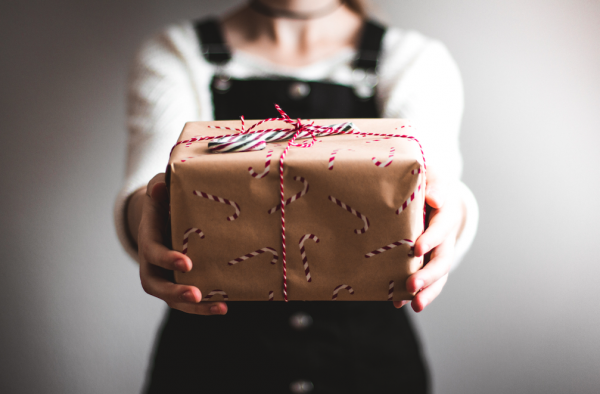 A lady holds out a holiday gift wrapped in hand printed brown paper