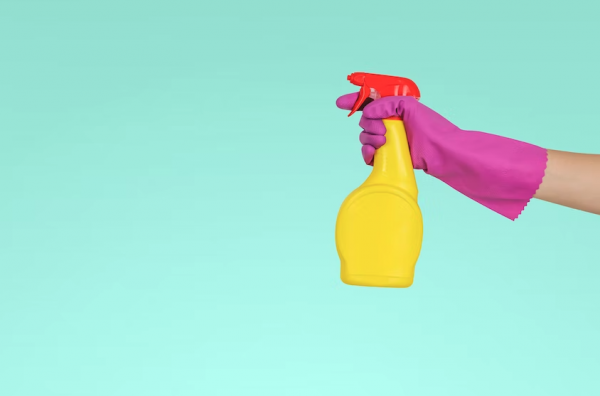 Spring clean your ESG strategy - a hand in a pink rubber glove holds a yellow spray bottle in front of a light green background.