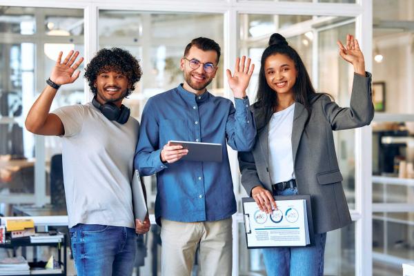 Three smiling employees waving during a CSR onboarding session in a modern office, representing internal CSR examples and how CSR in recruitment helps engage new employees.