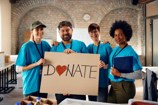 workplace donation matching, A group of corporate volunteers with a sign inviting people to donate