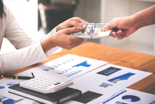 Hands exchanging money over charts to improve workplace giving as a part of a company's payroll giving policy.